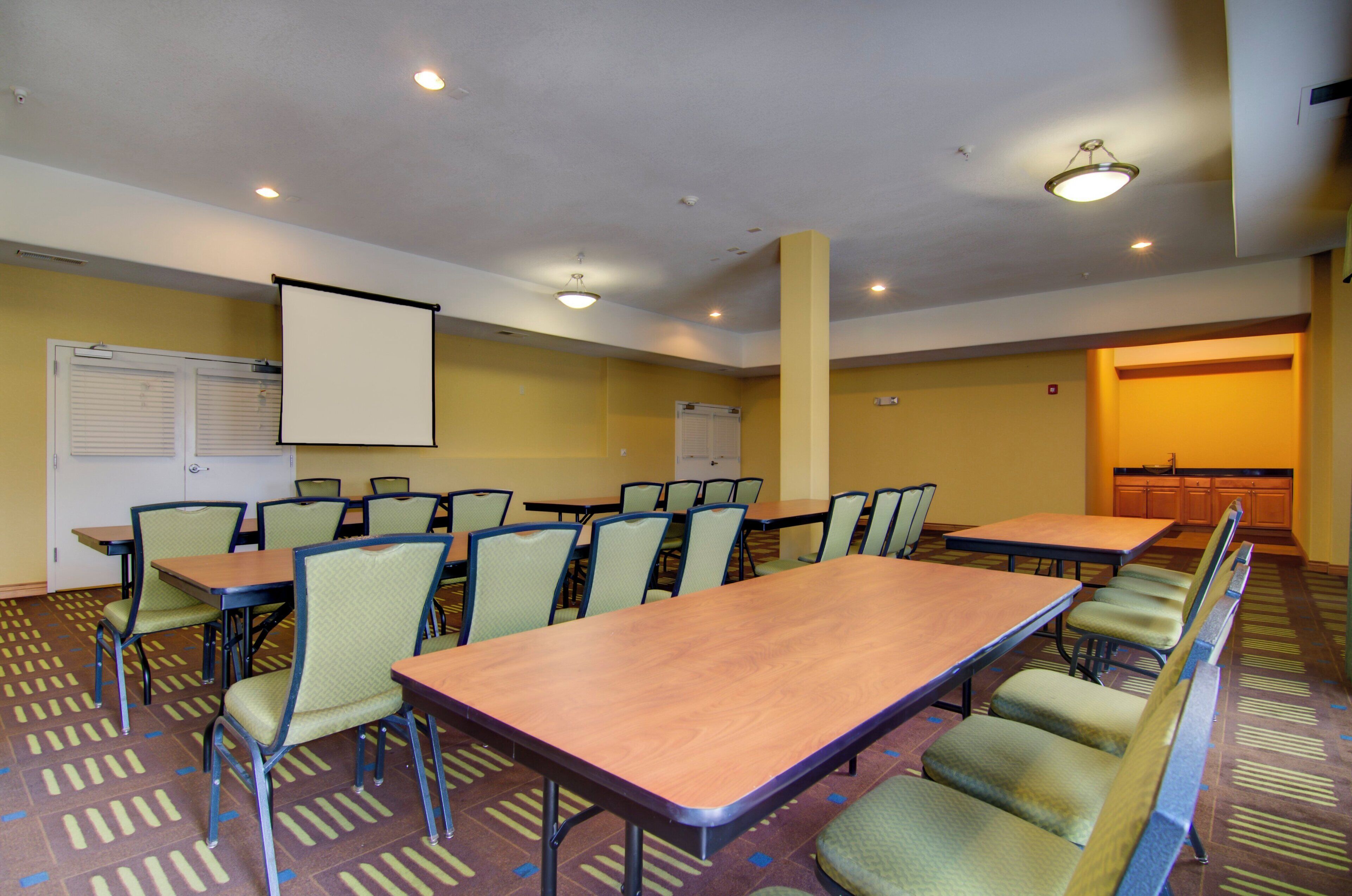 A conference room with tables and chairs, a projector screen, and a whiteboard.