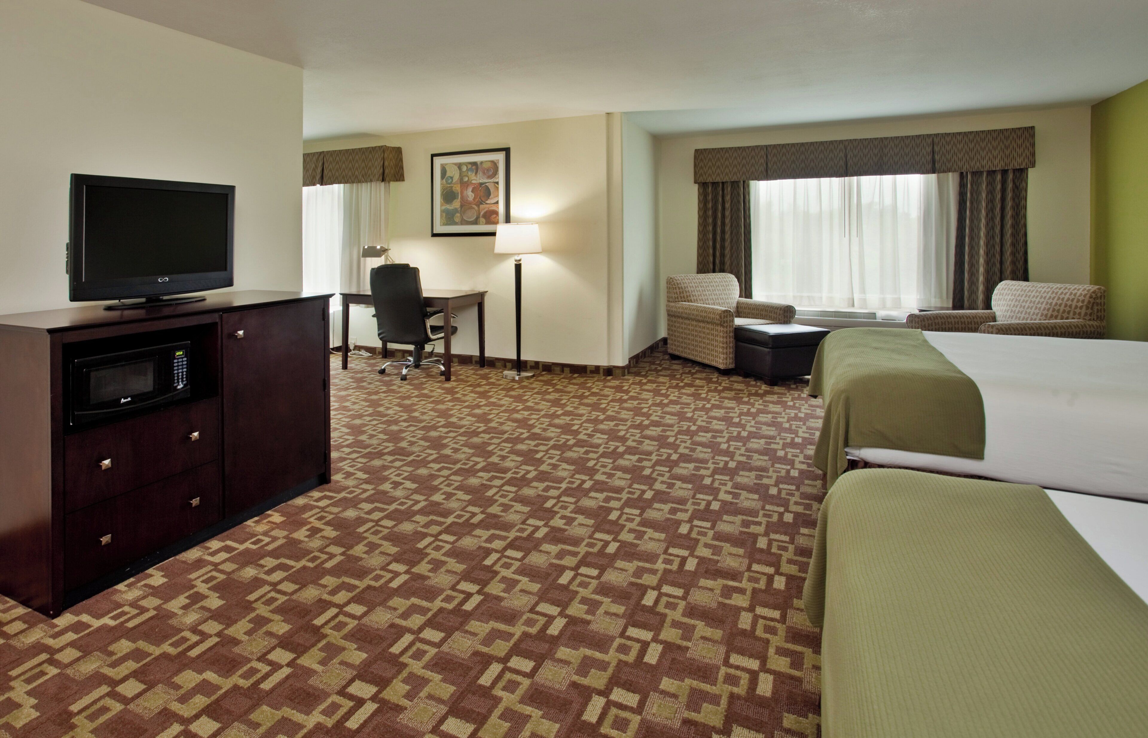 A hotel room with a bed, a desk, a chair, a television, and a lamp.