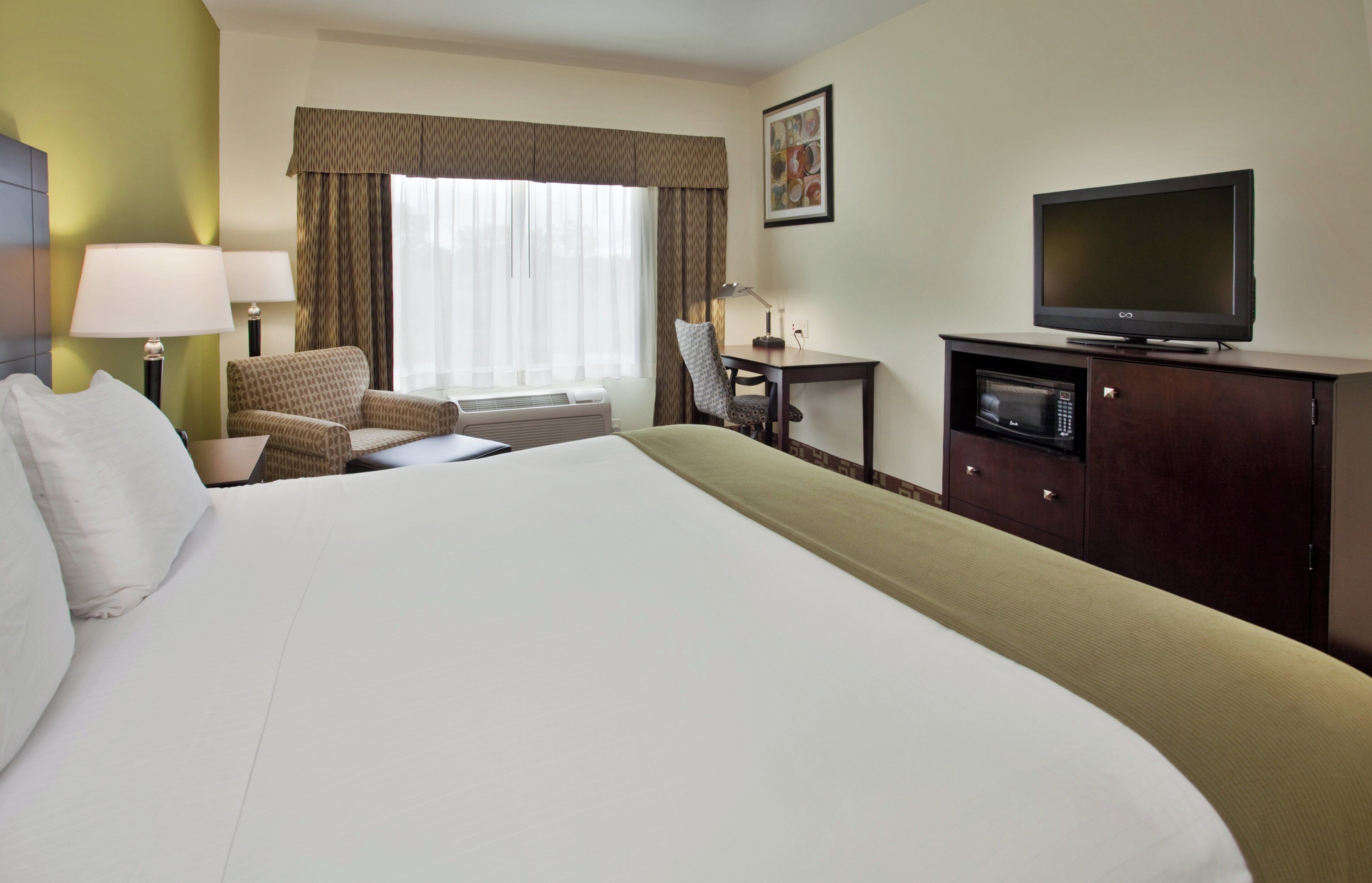 A hotel room with a large bed, a desk with a chair, a television, and a window with curtains.