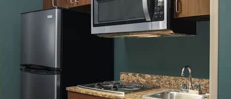 Una cocina con refrigerador de acero inoxidable, microondas, estufa a gas y un lavamanos.