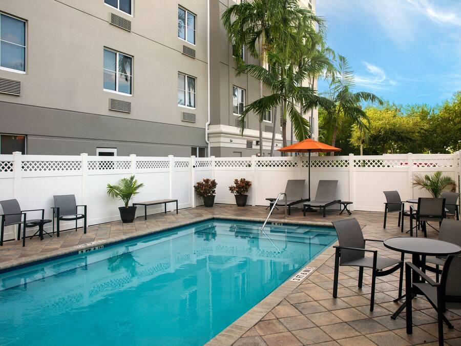 A swimming pool with lounge chairs and tables, surrounded by a white fence and potted plants.