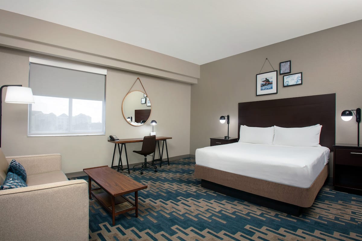 A hotel room with a bed, desk, chair, and a sofa.
