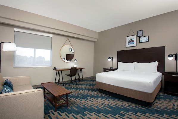 A hotel room with a bed, desk, chair, and a sofa.