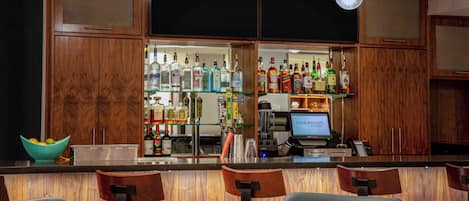 Zona de bar con armarios de madera, un monitor de computadora y diversas botellas de licor.