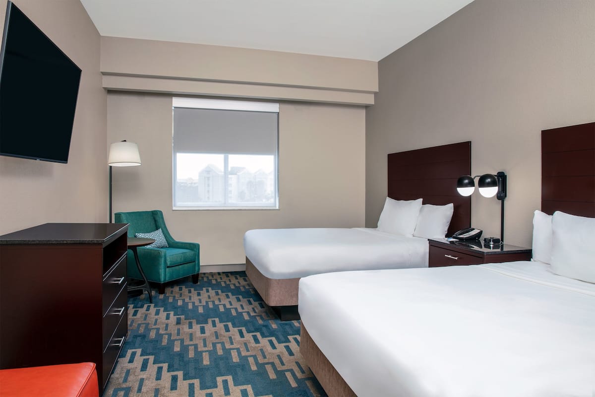 A hotel room with two beds, a desk, a chair, a TV, and a window with a city view.