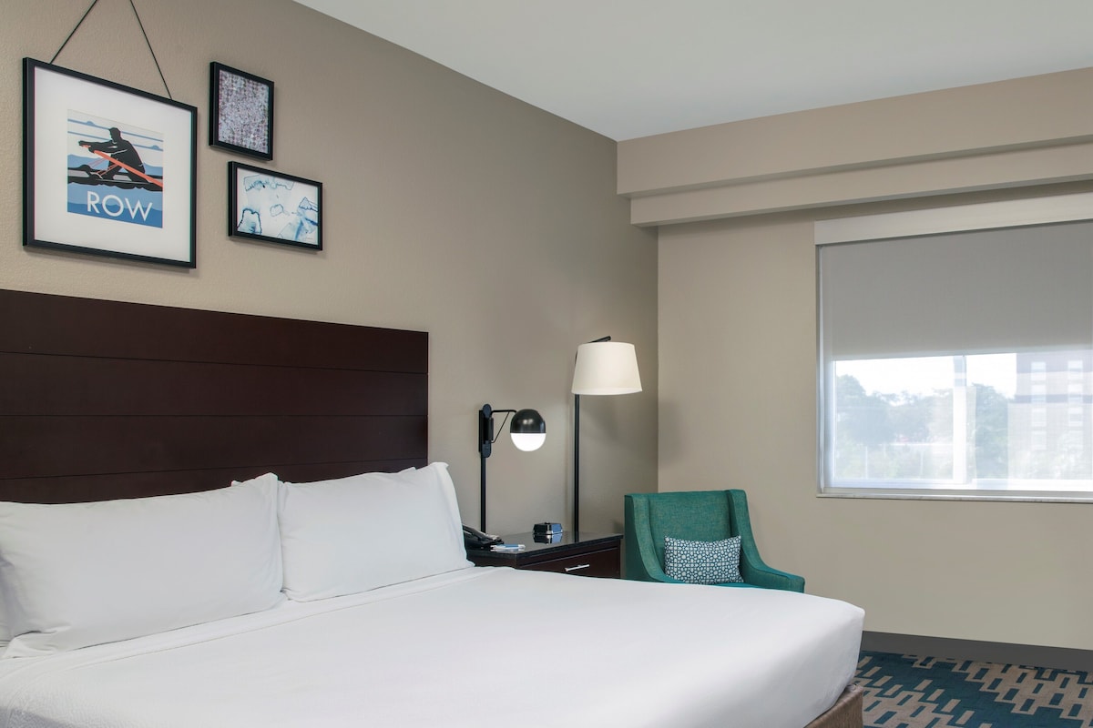 A hotel room with a large bed, a desk with a lamp, a chair, and framed pictures on the wall.