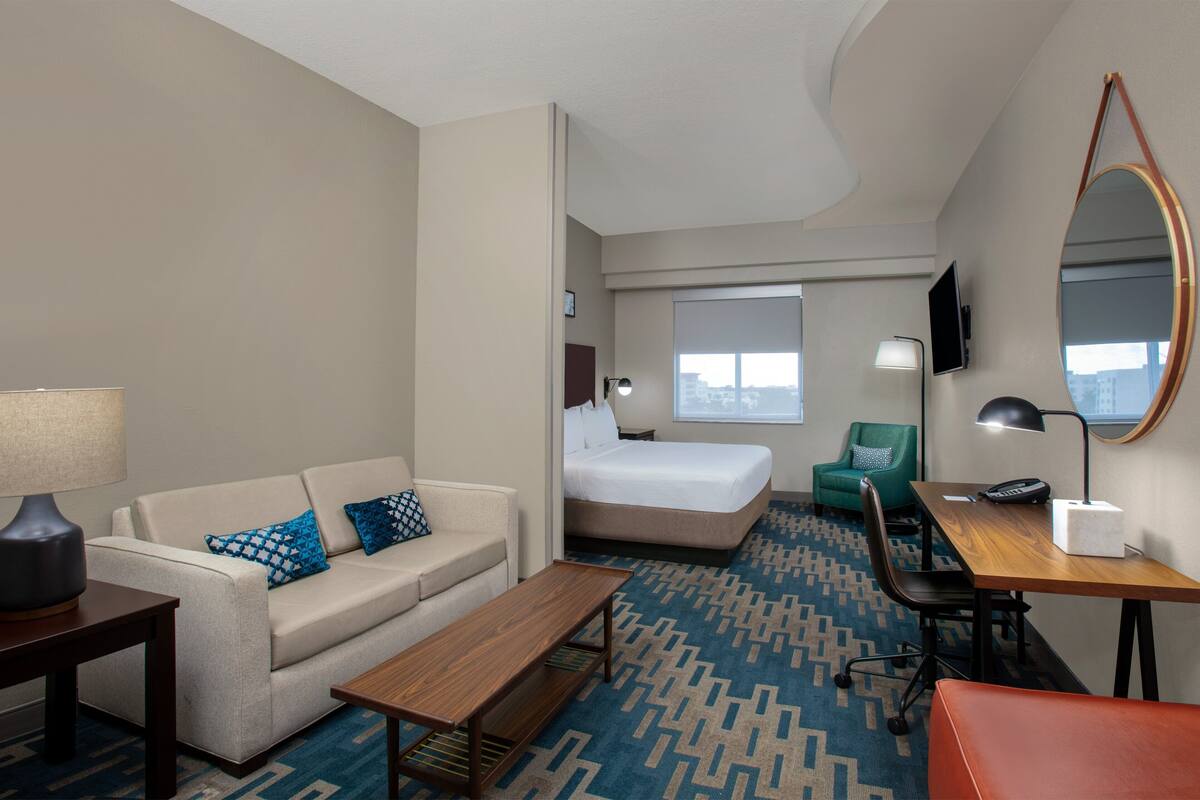 A hotel room with a sofa, a bed, a desk, a mirror, and a TV.