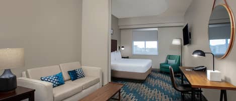 A hotel room with a sofa, a bed, a desk, a mirror, and a TV.