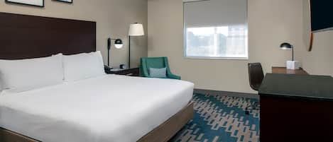 Une chambre d’hôtel avec un grand lit, un bureau, une chaise, une fenêtre et des tableaux encadrés au mur.