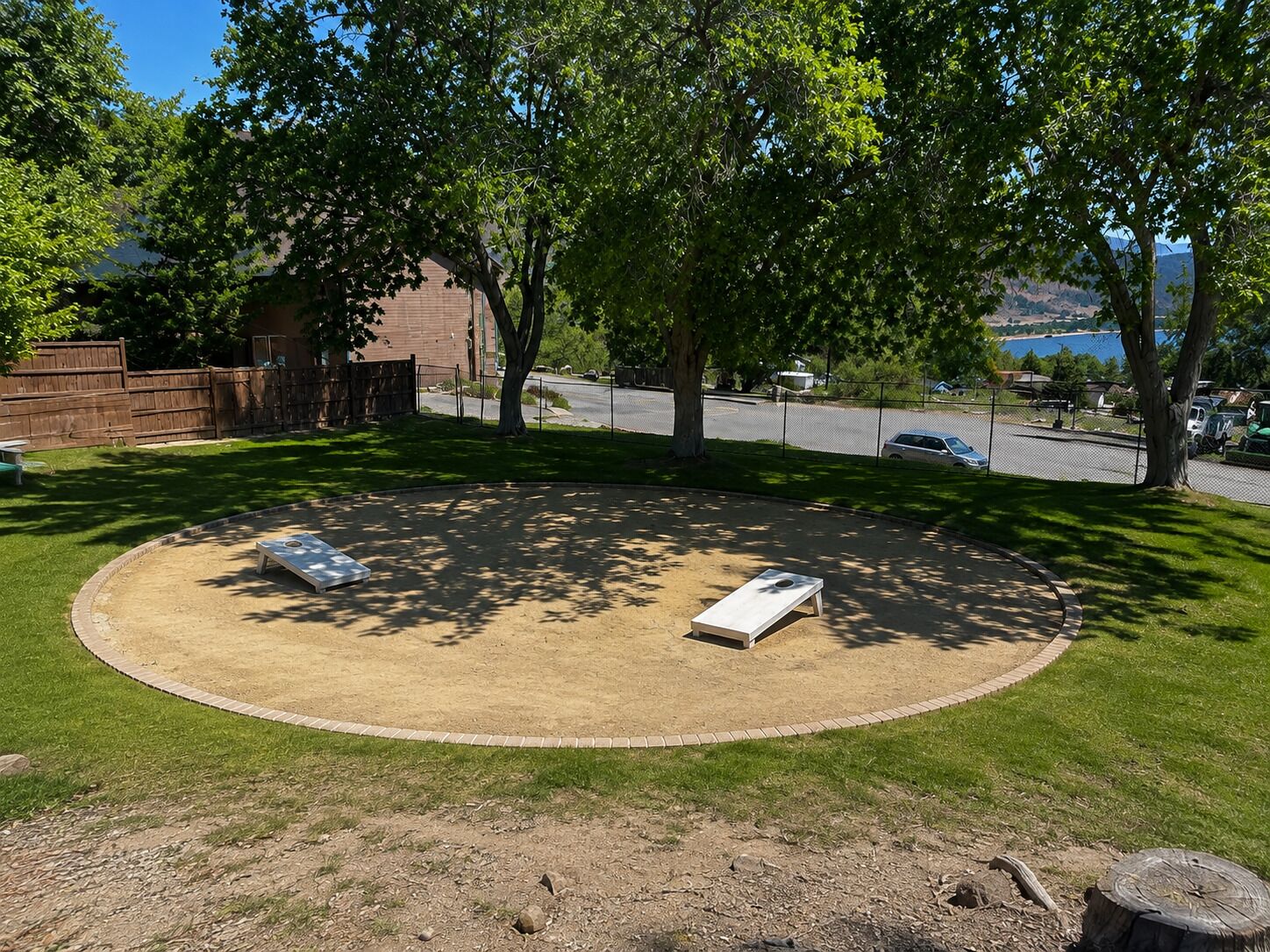 Un’area esterna circolare con due panchine, circondata da erba e alberi, con vista su un corpo d'acqua e un parcheggio sullo sfondo.