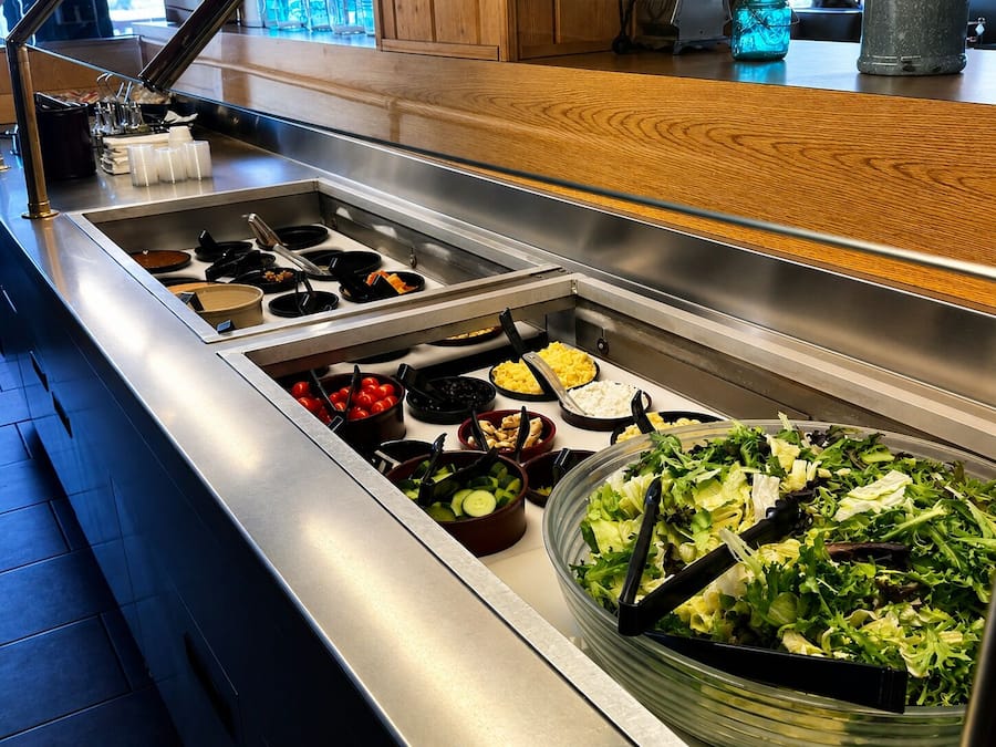 Buffet com diversas estações de comida, incluindo saladas, pratos quentes e uma variedade de acompanhamentos.