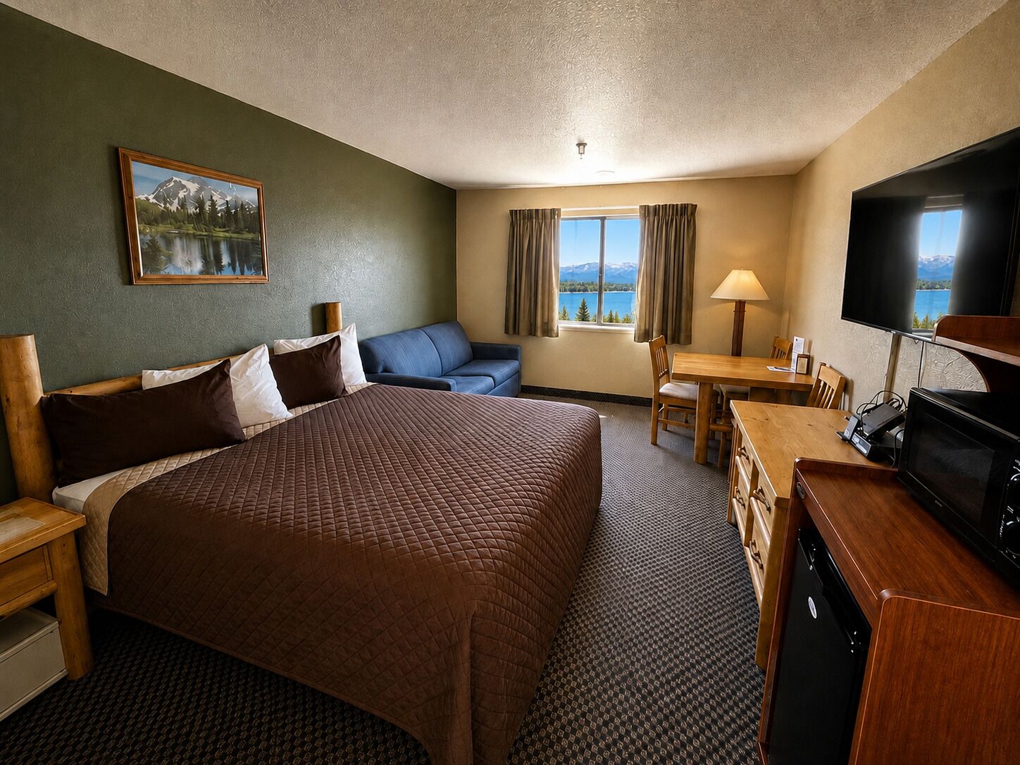 A hotel room with a large bed, a sofa, a desk with a TV, and a window with curtains.