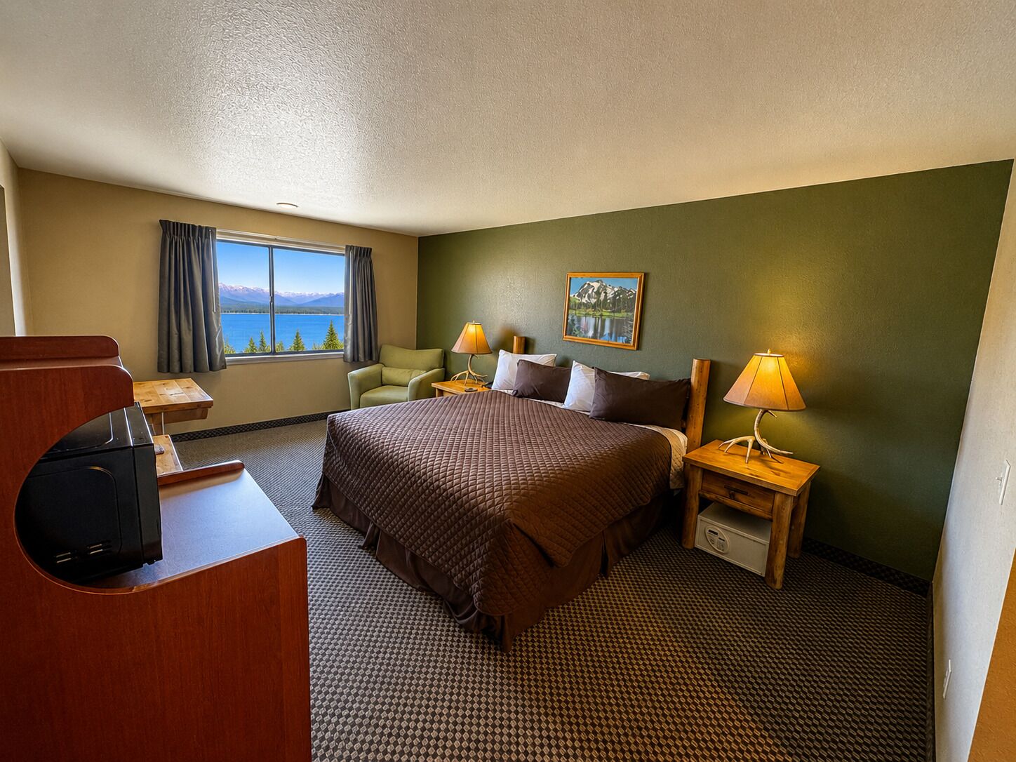 A hotel room with a bed, a desk, a chair, a lamp, and a painting.