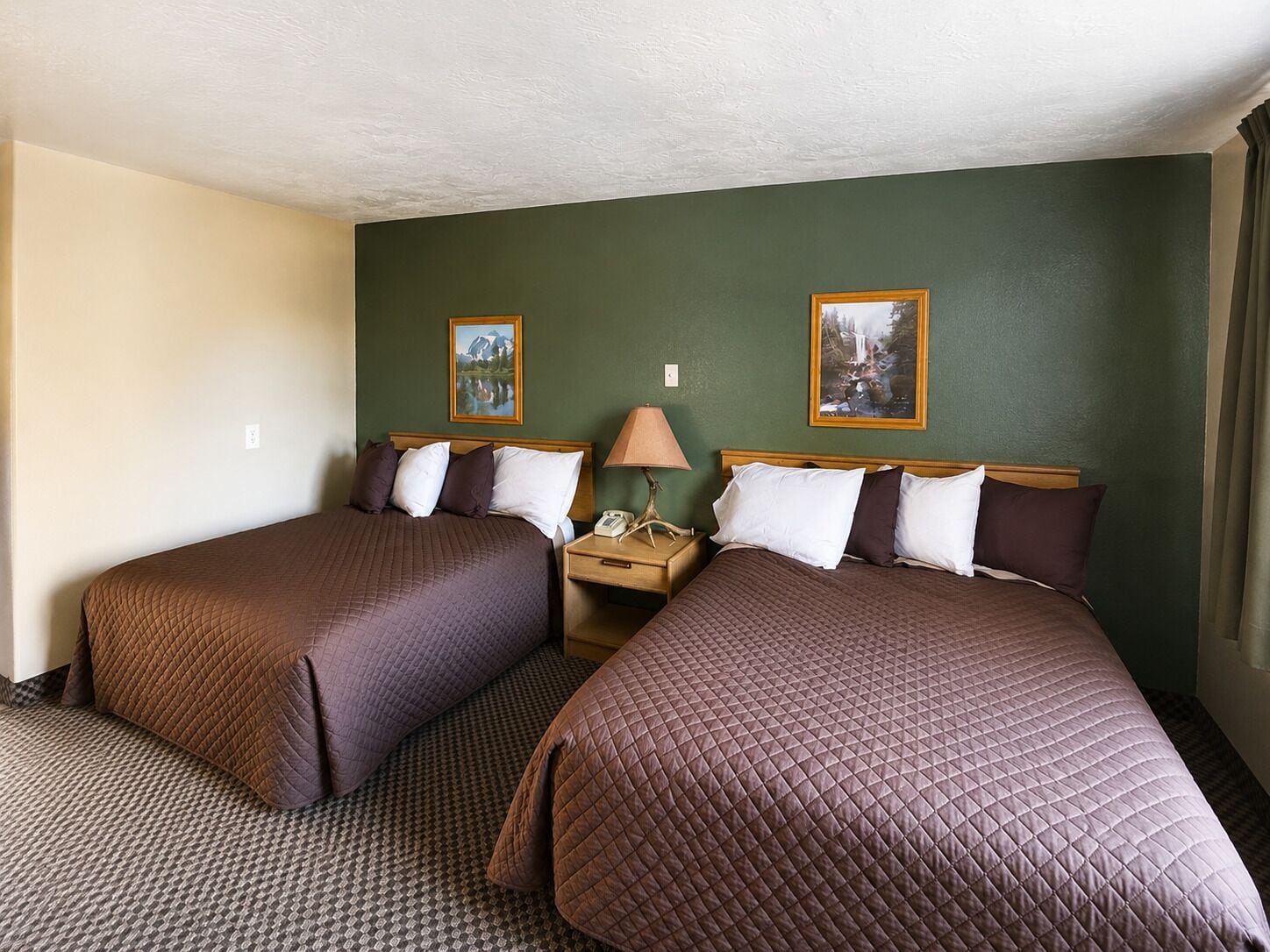 A hotel room with two beds, a nightstand with a lamp, and two framed pictures on the wall.