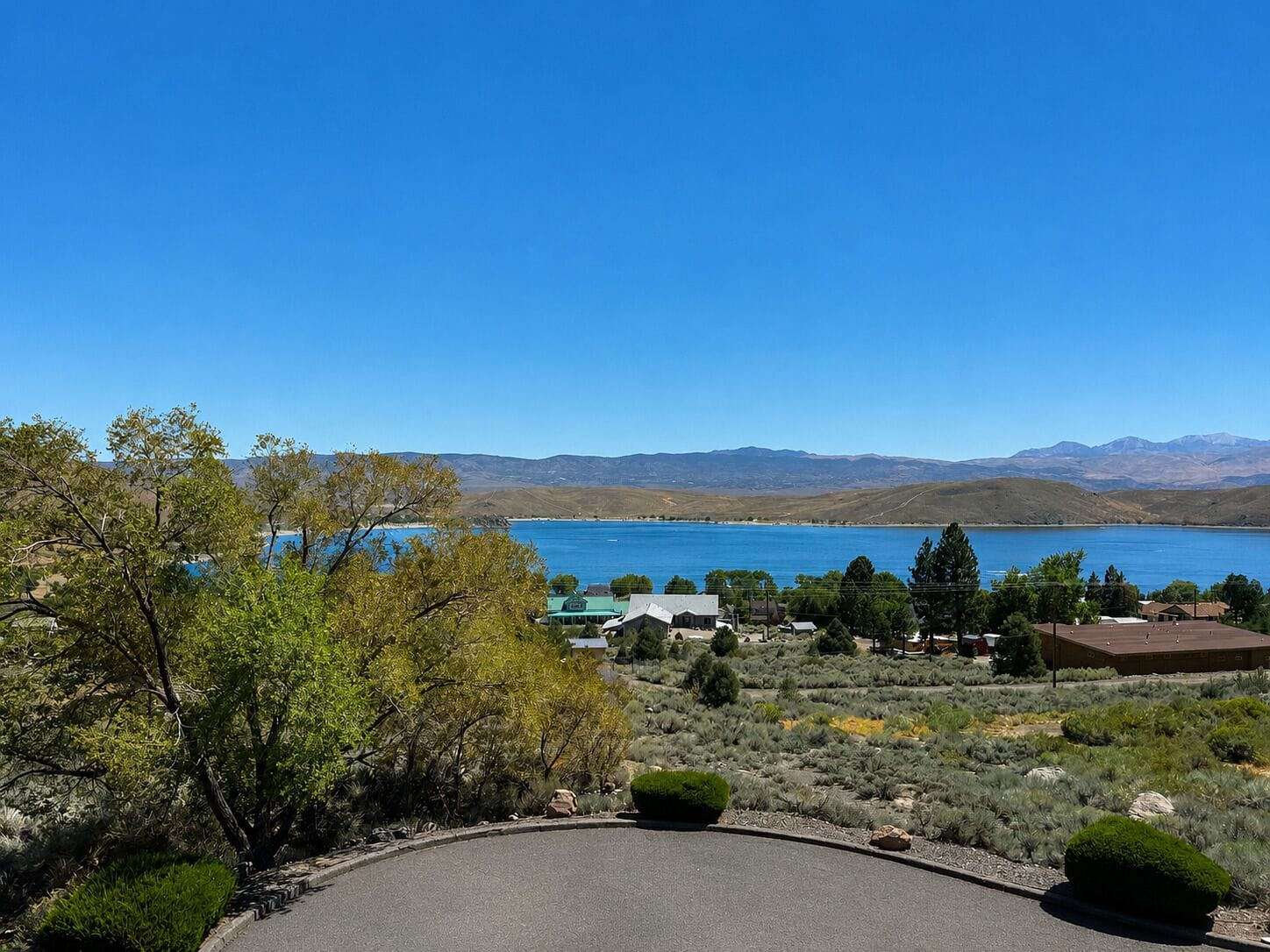 Une vue pittoresque d’un lac, avec des montagnes en arrière-plan, le tout entouré de jardins aménagés et de bâtiments.
