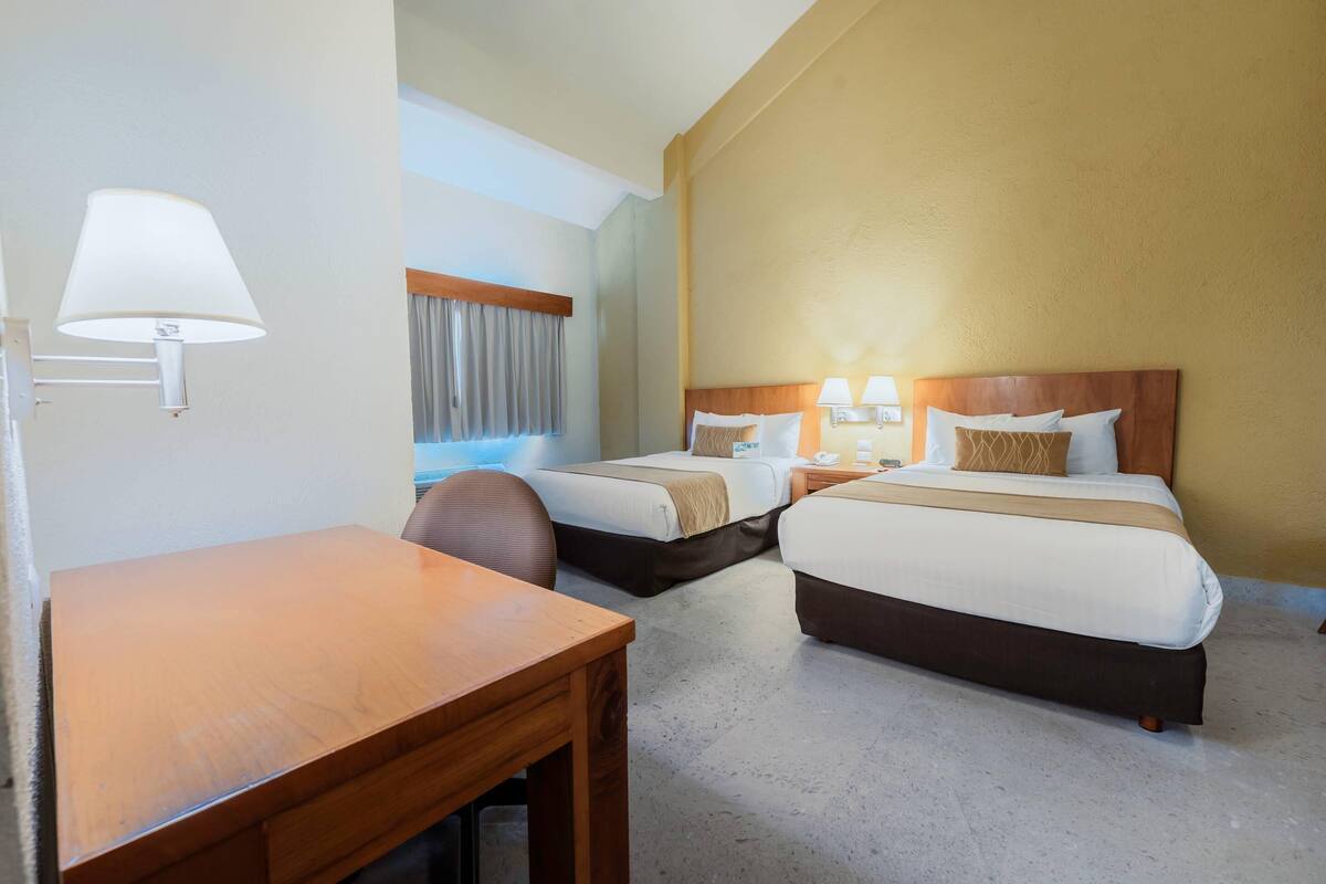 Ein Hotelzimmer mit zwei Betten, einem Schreibtisch und einem Stuhl.