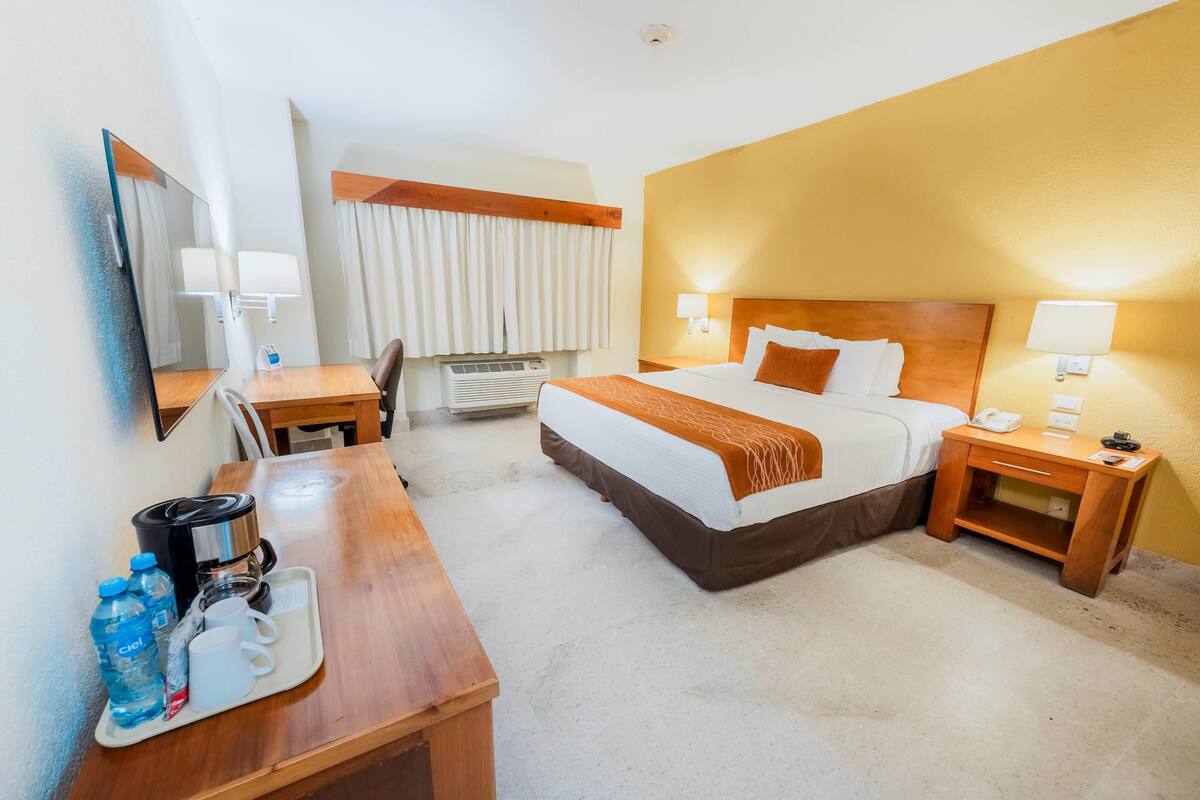 Ein Hotelzimmer mit Bett, Nachttischen, einem Schreibtisch mit Kaffeemaschine und einem Spiegel.