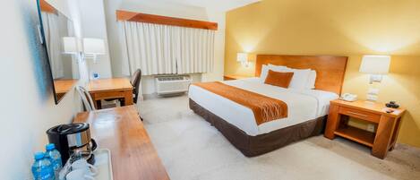 Una habitación de hotel con cama, mesitas de noche, un escritorio con cafetera y un espejo.