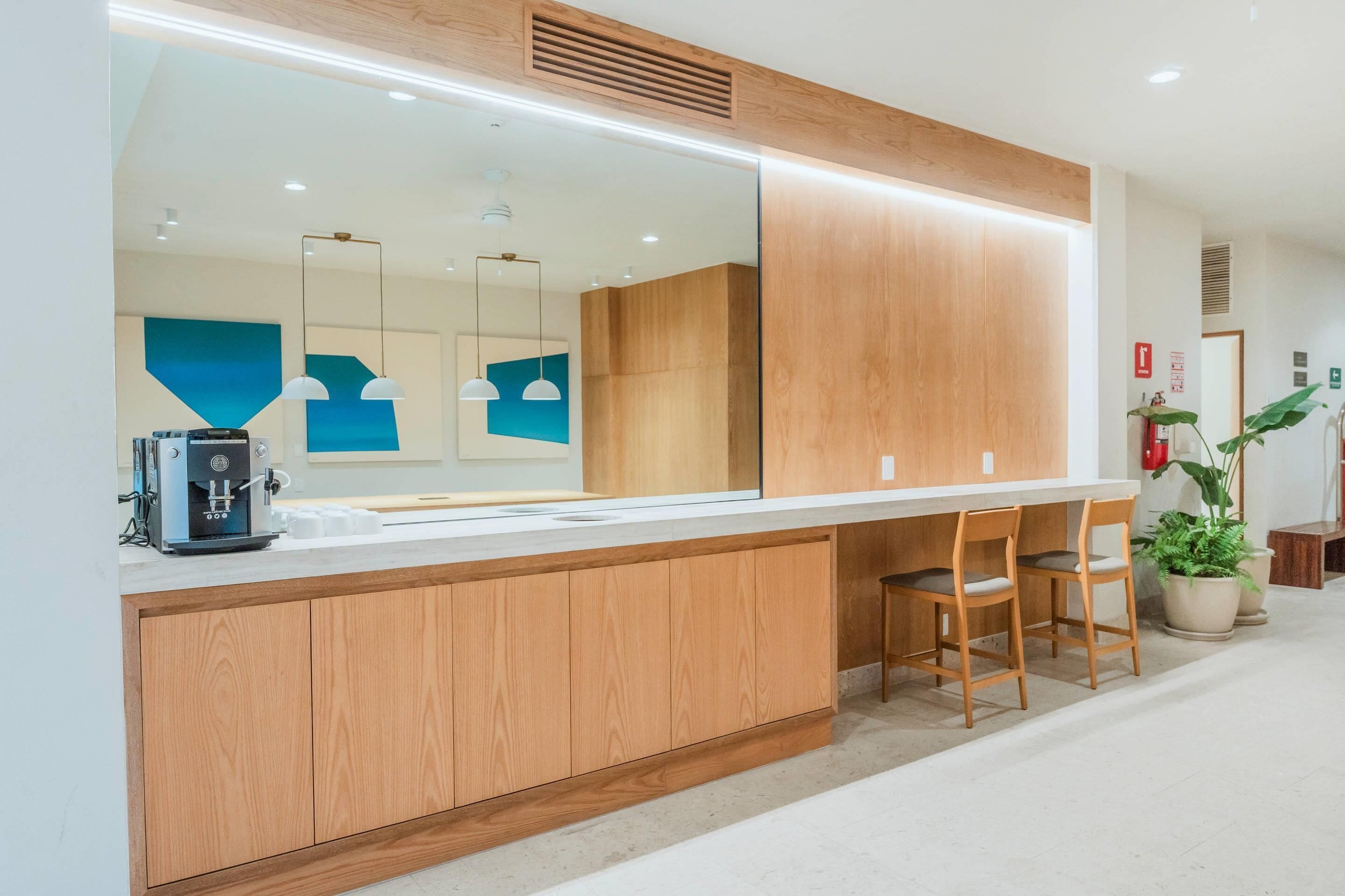 Una moderna zona de recepción con mostrador de madera, dos sillas, una máquina de café y un espejo grande.