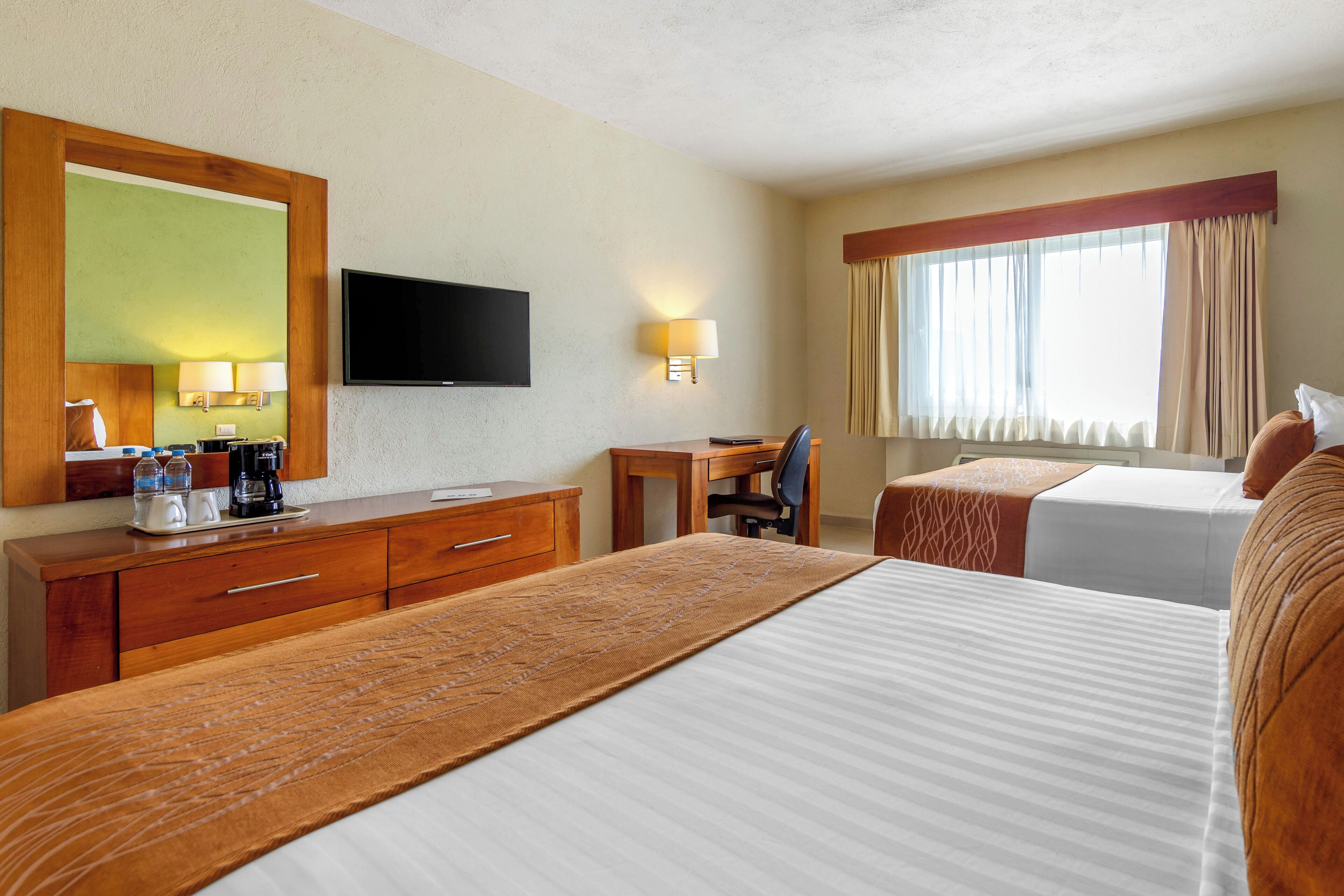 A hotel room with a large bed, a desk with a chair, a television, and a window with curtains.
