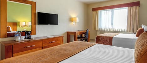 Habitación de hotel con una cama grande, un escritorio con silla, televisor y ventana con cortinas.