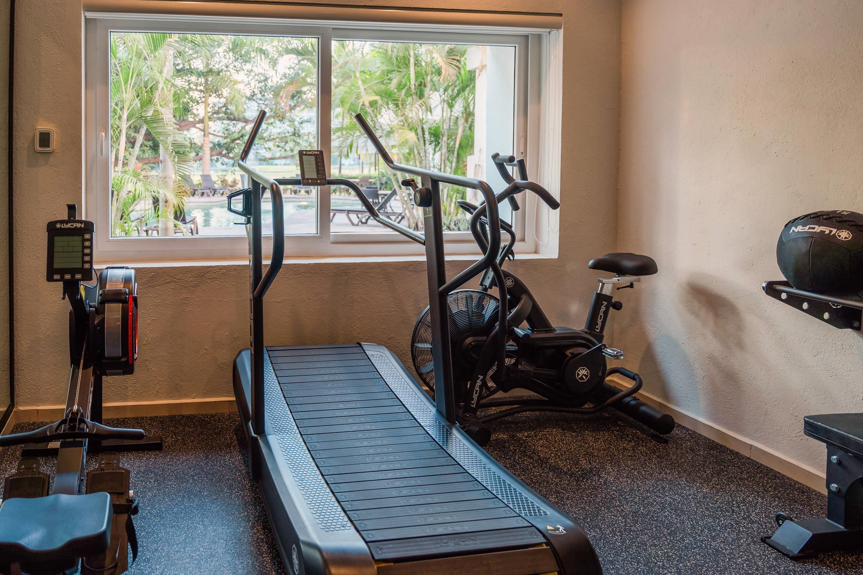 Een fitnessruimte met een loopband, hometrainer en roeimachine.