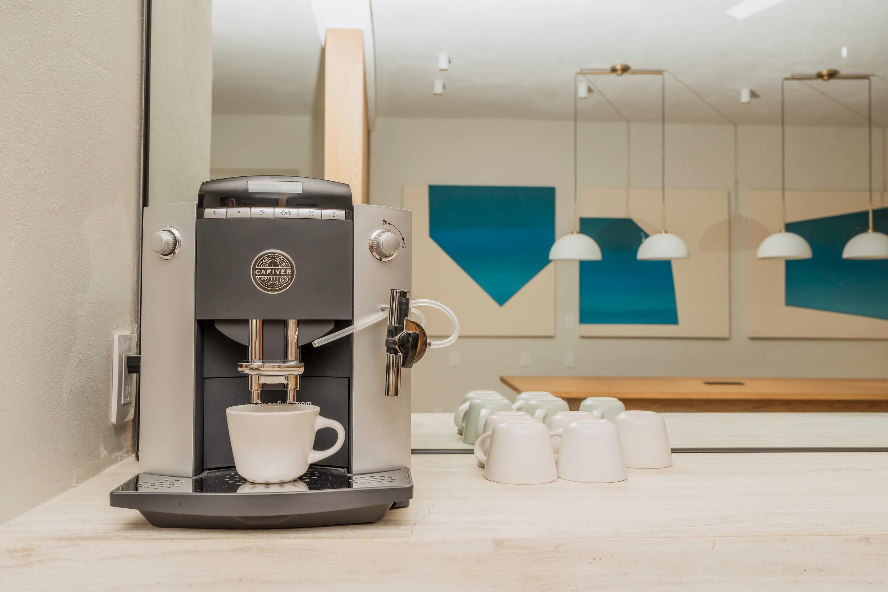 Una cafetera moderna con una taza de café, un espejo y una pared con decoración geométrica.