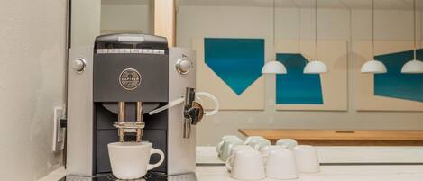 Una cafetera moderna con una taza de café, un espejo y una pared con decoración geométrica.