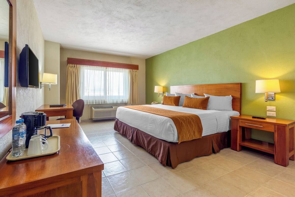 Ein Hotelzimmer mit Bett, Nachttischen, einem Schreibtisch mit Kaffeemaschine und einem Fernseher.