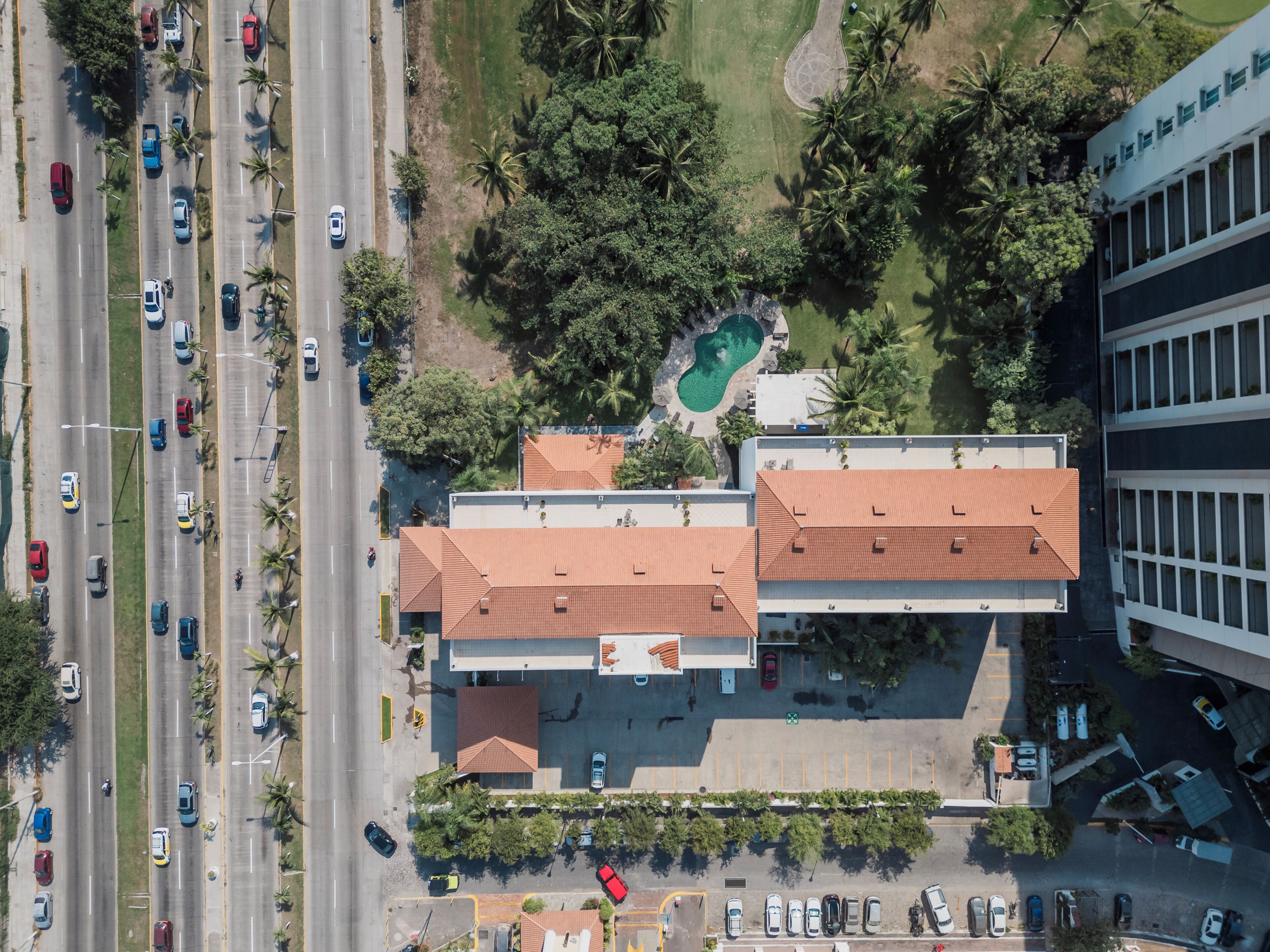 An aerial view of a building with a swimming pool, parking lot, and a road with vehicles.