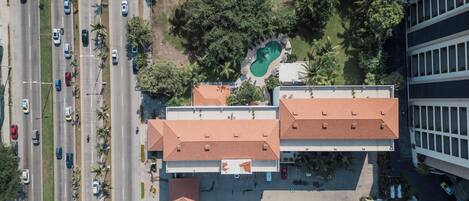 An aerial view of a building with a swimming pool, parking lot, and a road with vehicles.