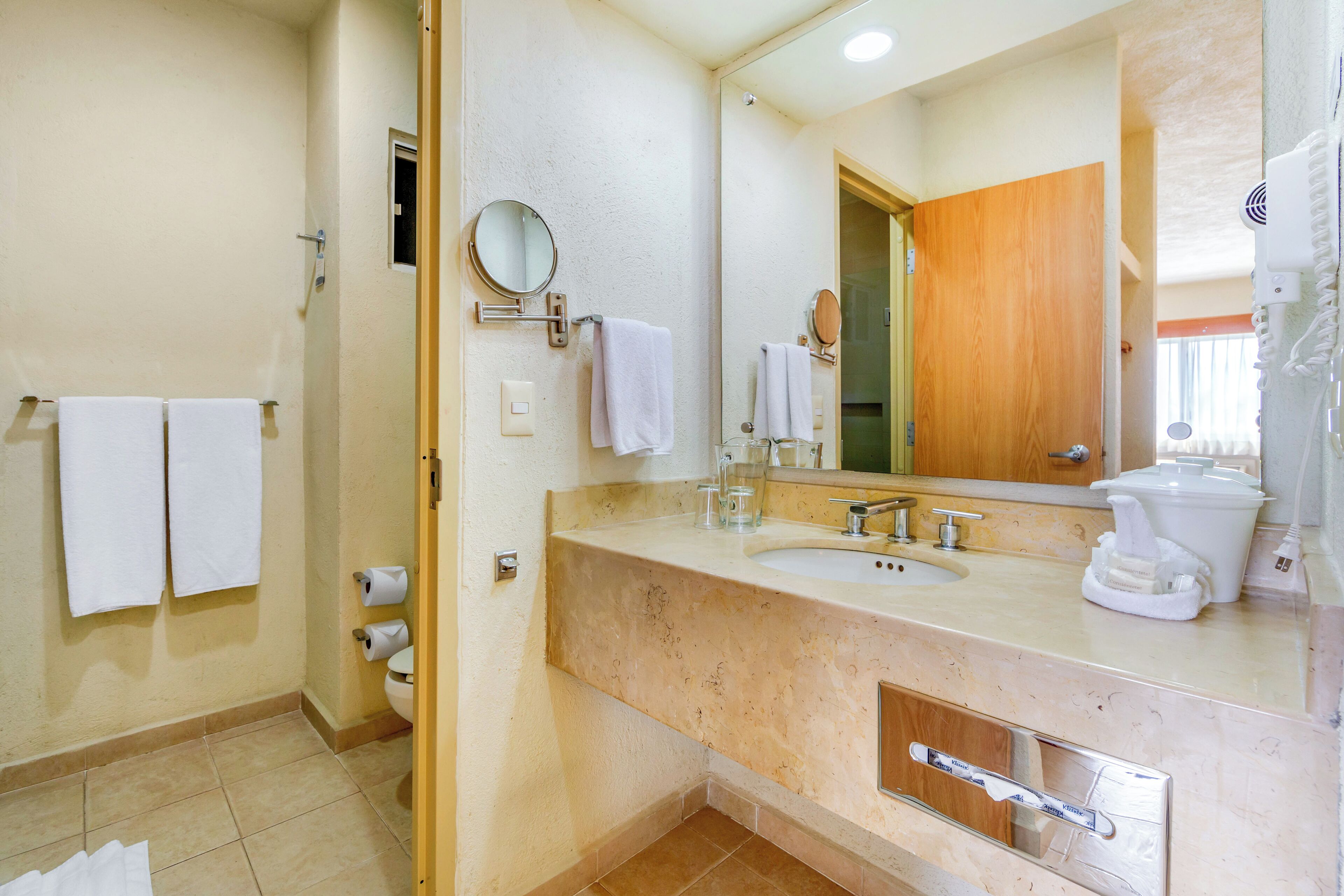 A bathroom with a beige countertop, a sink, a mirror, and two white towels hanging on the wall.