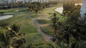 Play a round of golf amidst lush greenery and palm trees, with modern high-rise buildings in the background.