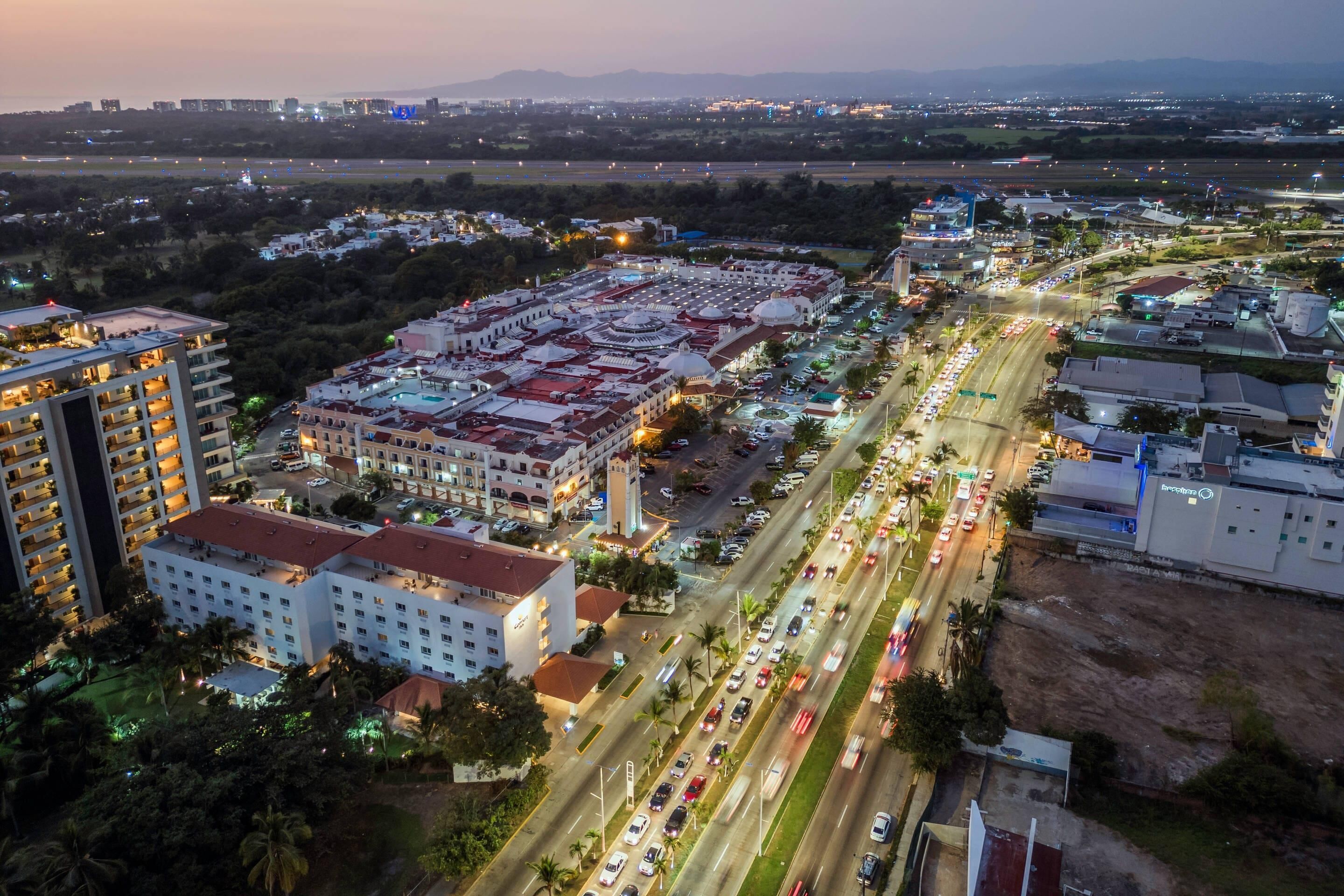 An aerial view of a hotel complex with multiple buildings, a parking area, and a busy road with vehicles.
