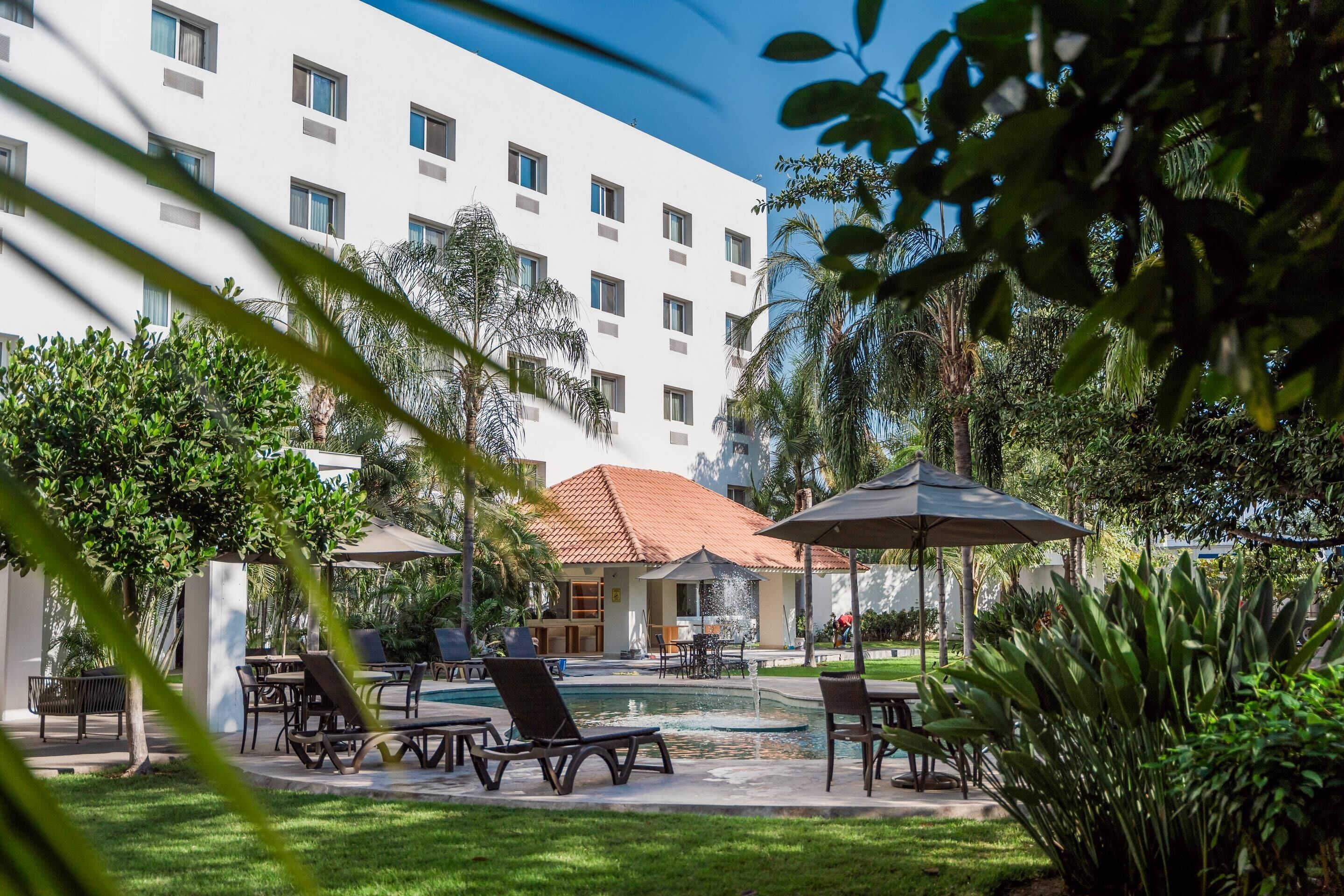 A courtyard with a swimming pool, lounge chairs, and umbrellas.