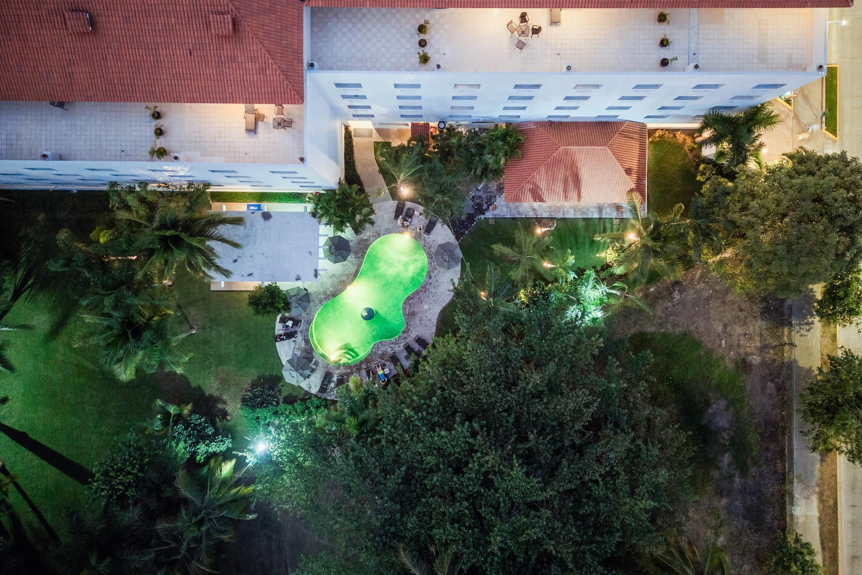 An aerial view of a hotel courtyard with a swimming pool, surrounded by lush greenery and palm trees.