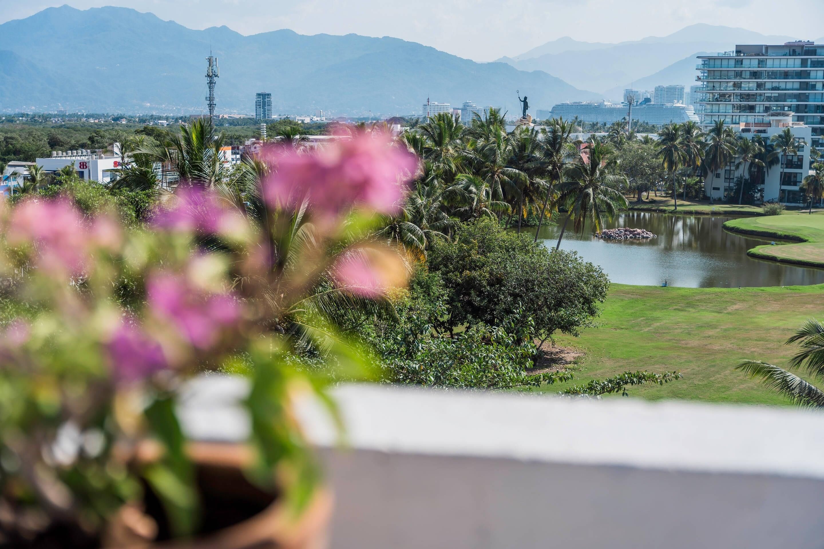 A view of a cityscape with mountains in the background, a body of water, and a statue on a hill.