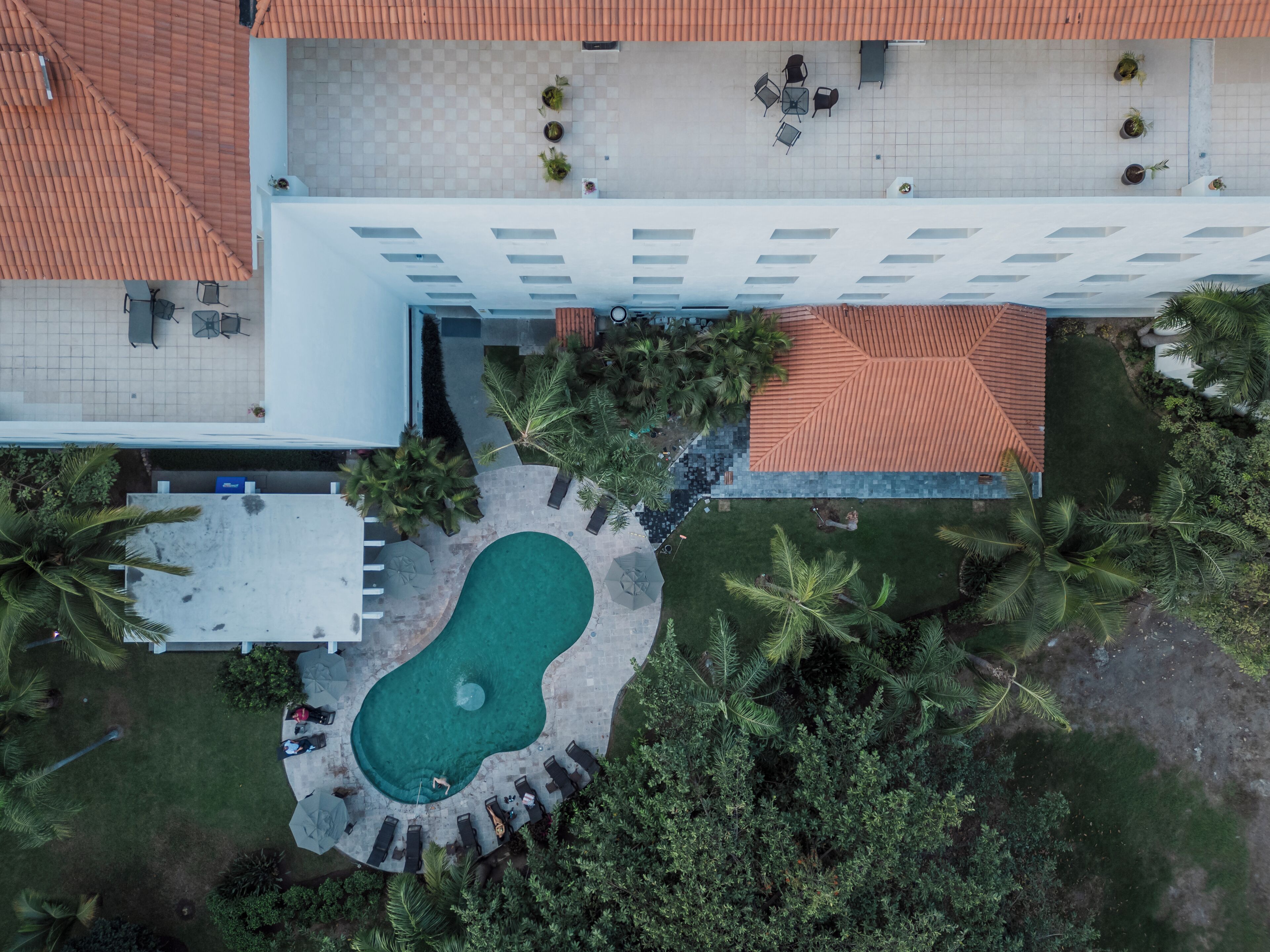 Luftaufnahme eines Hotels mit Schwimmbad, Sitzgelegenheiten im Freien und Palmen.