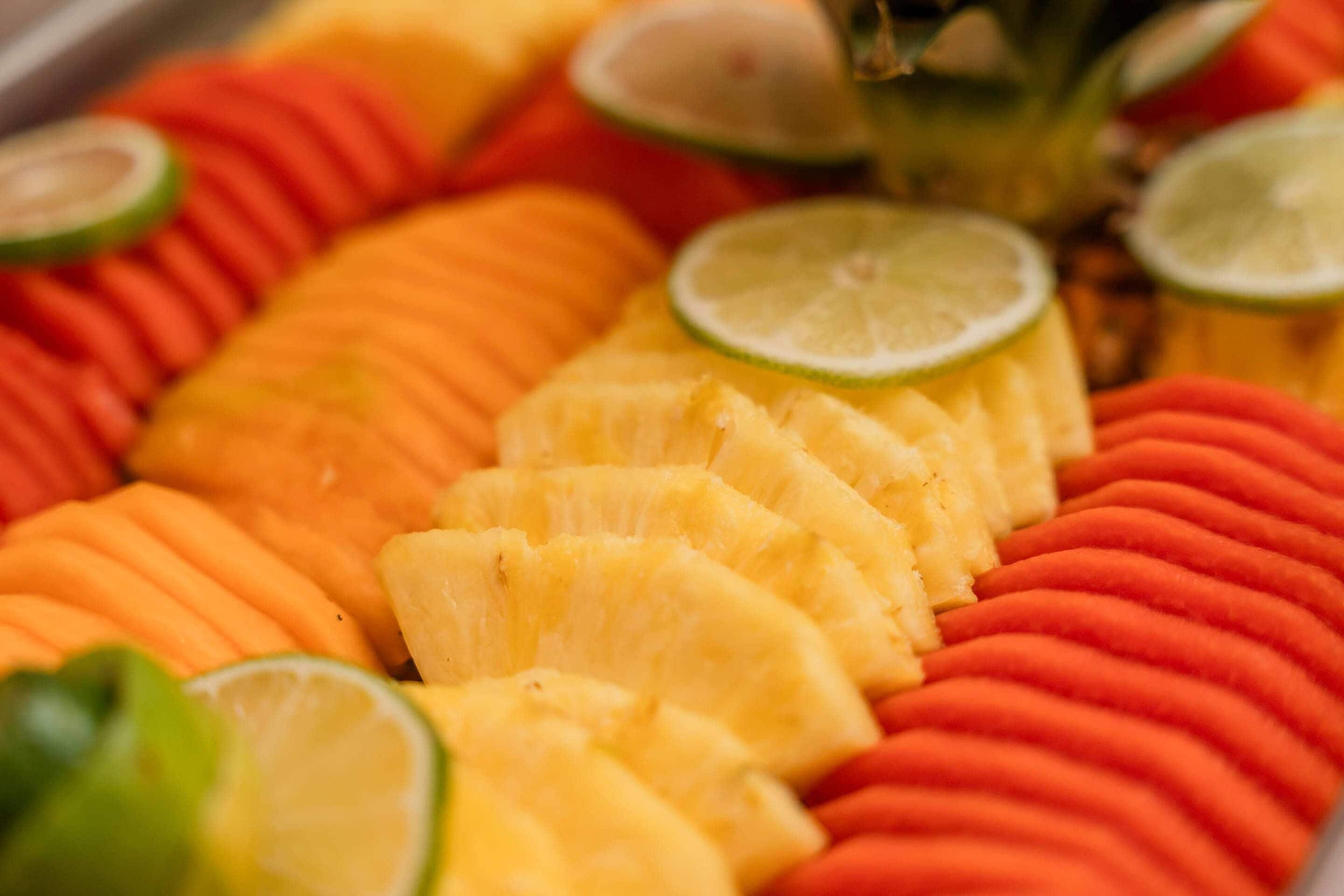 A fruit platter with pineapple, mango, and orange slices, garnished with lime wedges.