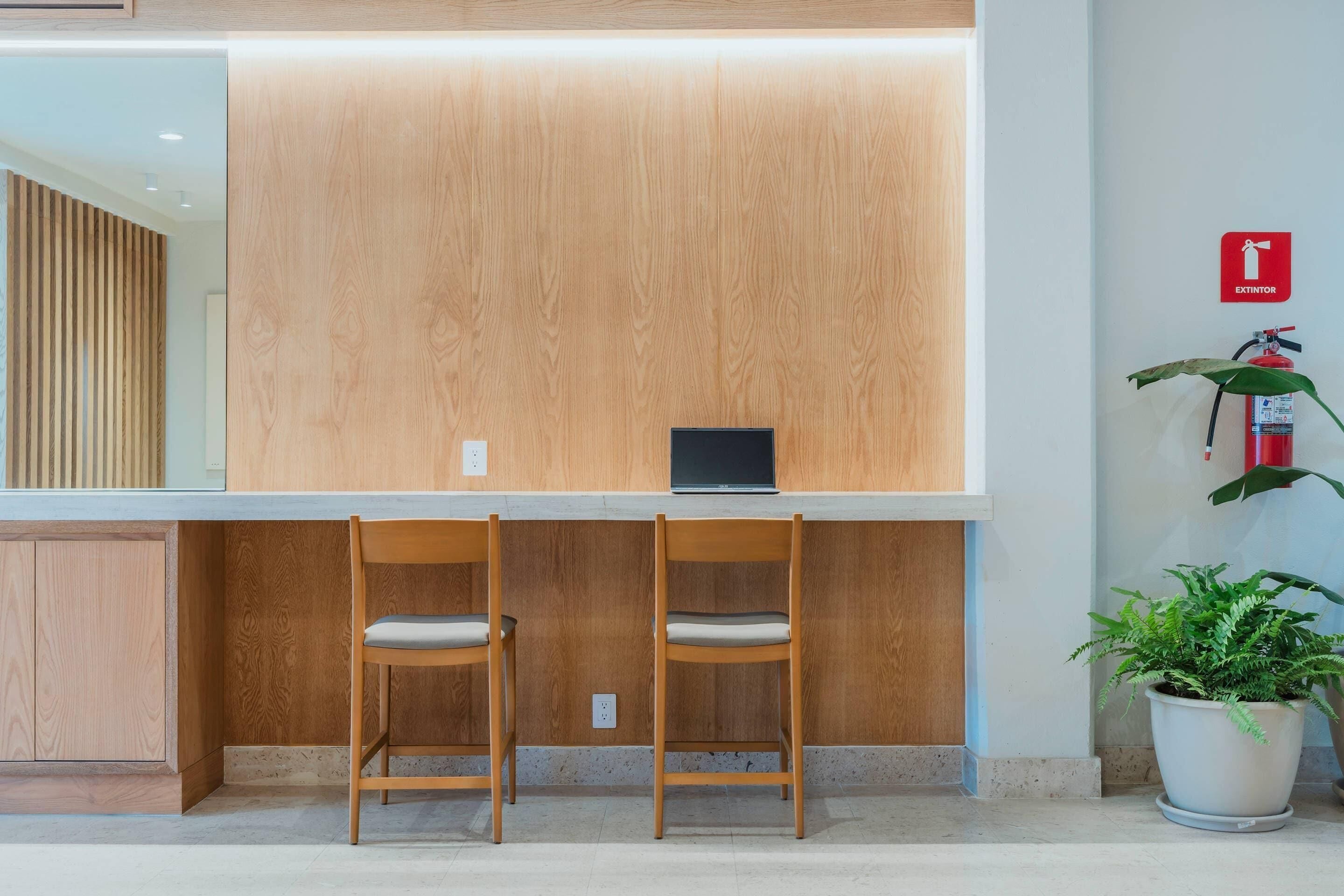 Un mostrador de recepción con dos sillas de madera, una computadora portátil y una planta en maceta.