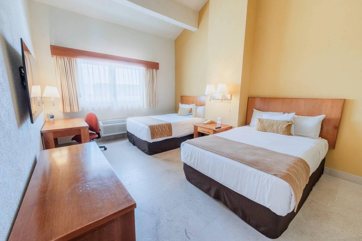 Ein Hotelzimmer mit zwei Betten, einem Schreibtisch, einem Sessel und einem Fernseher.