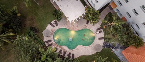An aerial view of a hotel with a swimming pool surrounded by palm trees and lounge chairs.