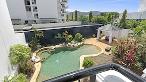 Una piscina en la azotea con agua cristalina, rodeada de plantas y rocas, y un pabellón.