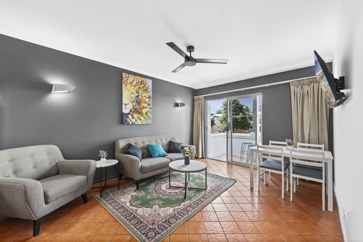 Un salon moderne avec des murs gris, un ventilateur de plafond, un canapé, une table basse et un téléviseur fixé au mur.