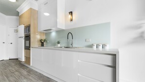 Una cocina moderna con armarios blancos, horno empotrado y un lavamanos de acero inoxidable.