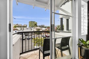 En balkon med to stole, en potteplante og udsigt til en parkeringsplads og bygninger.