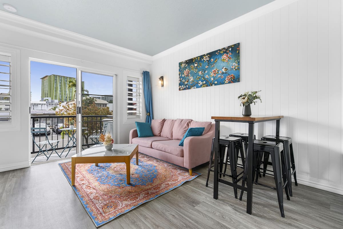 Un salon moderne avec un canapé rose, une table basse en bois et un tapis à motifs bleus.