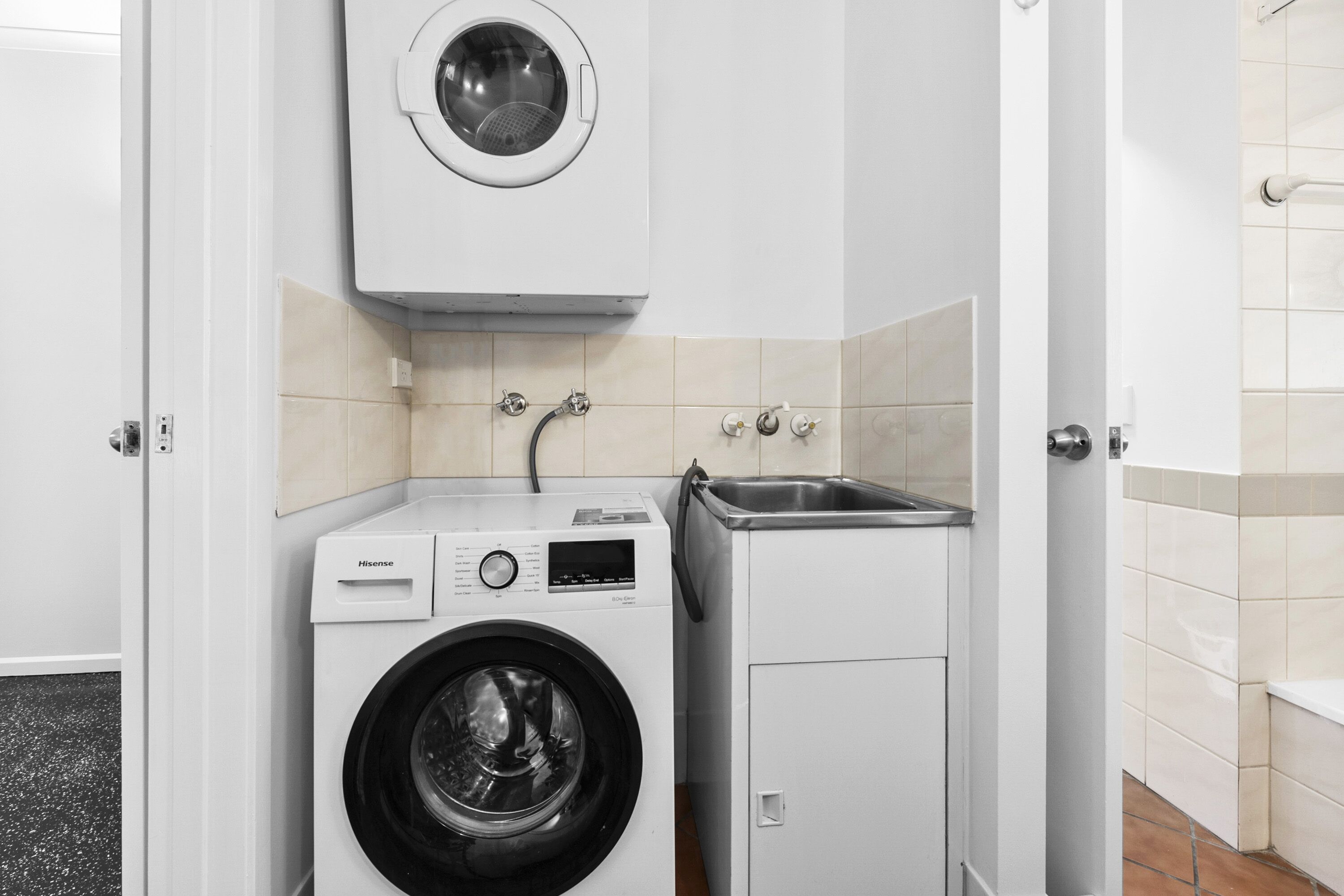 A compact laundry area with a front-loading washing machine, a built-in dryer, and a small sink.