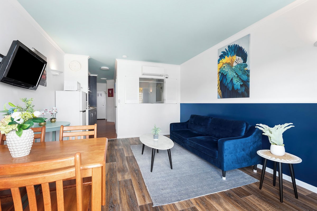 Un salon moderne avec un canapé bleu, une table à manger avec des chaises, une petite table basse et un téléviseur fixé au mur.