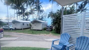 Een overdekt buitengebied met blauwe stoelen, uitzicht op palmbomen en stacaravans op de achtergrond.